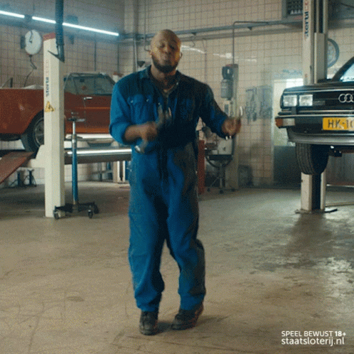 A Man In Blue Overalls Is Dancing In A Garage GIF