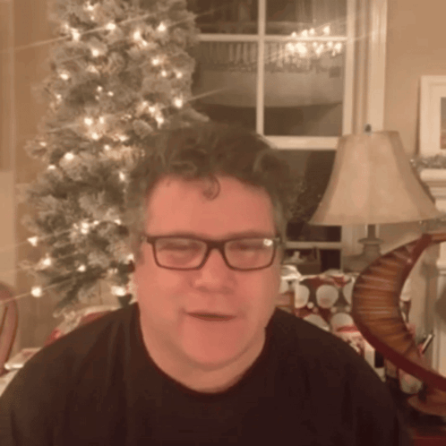 A Man In Front Of A Christmas Tree Wearing Glasses GIF