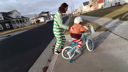 A Man In Green And White Striped Pajamas Helps A Little Girl Ride A Bike GIF
