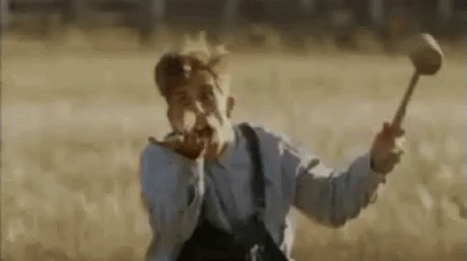 A Man In Overalls Is Holding A Hammer In A Field And Screaming . GIF