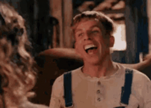 A Man In Overalls Is Laughing And Looking At A Woman . GIF