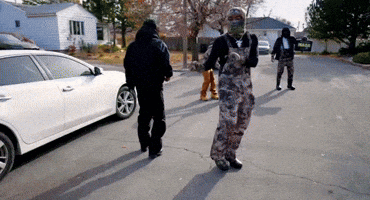 A Man In Overalls Is Walking Down A Street GIF
