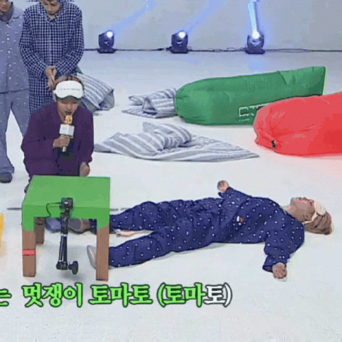 A Man In Pajamas Is Laying On The Floor With A Green Table In The Foreground GIF