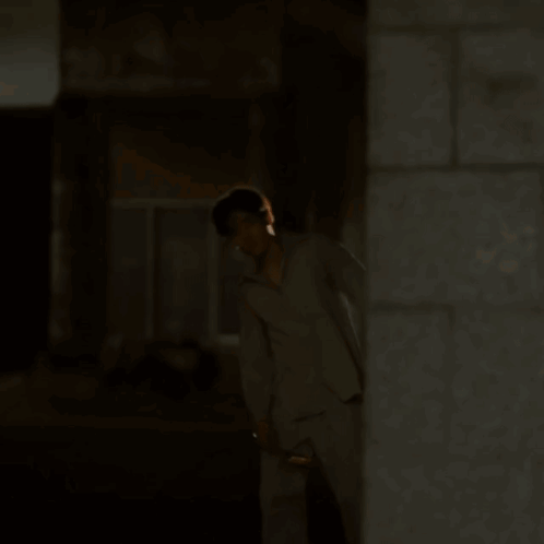 A Man In Pajamas Is Walking Down A Street At Night GIF