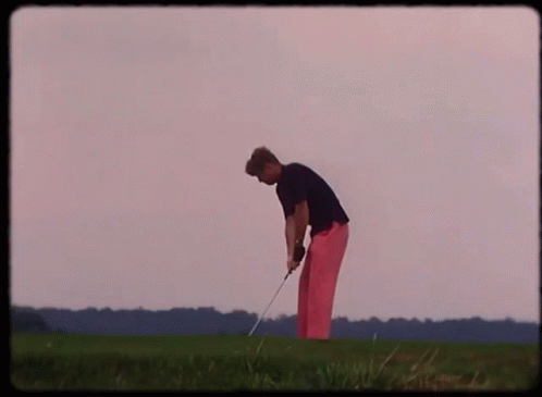 A Man In Pink Pants Is Swinging A Golf Club On A Green Field GIF