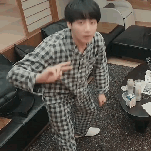 A Man In Plaid Pajamas Is Standing In A Living Room GIF