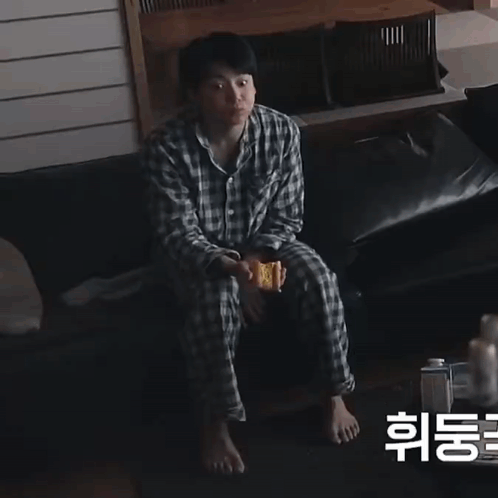 A Man In Plaid Pajamas Sits On A Couch Holding A Sandwich GIF