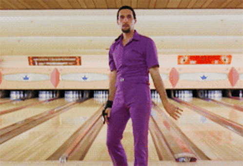 A Man In Purple Overalls Stands In A Bowling Alley GIF