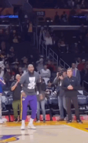 A Man In Purple Pants Is Standing On A Basketball Court In Front Of A Crowd Of People . GIF