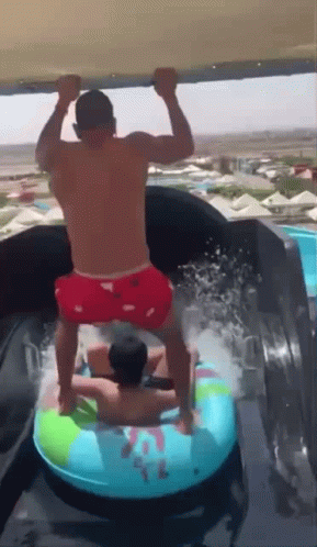 A Man In Red Shorts Is Standing On A Water Slide With Another Man GIF