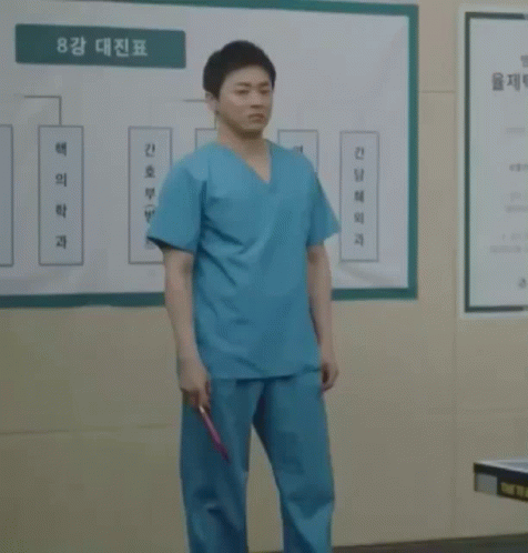 A Man In Scrubs Holds A Red Ping Pong Paddle GIF