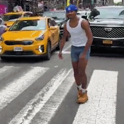 A Man In Shorts And A Tank Top Is Crossing A Street In Front Of A Yellow Car . GIF