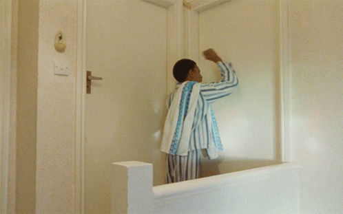 A Man In Striped Pajamas Stands In Front Of A White Door GIF