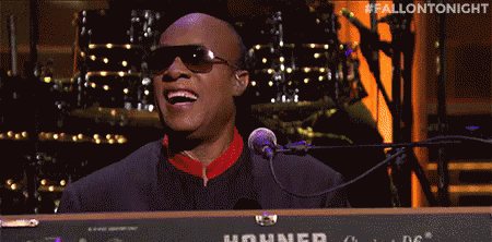 A Man In Sunglasses Is Singing Into A Microphone While Playing A Keyboard . GIF