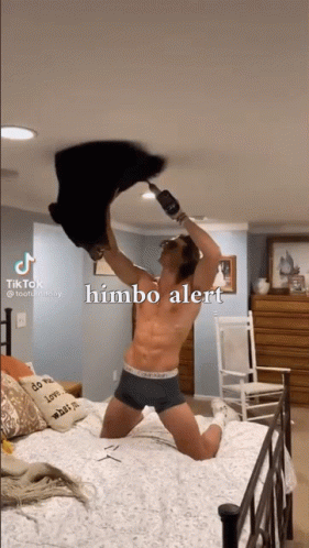 A Man In Underwear Is Kneeling On A Bed With A Bottle Of Wine In His Hand And The Caption Himbo Alert GIF