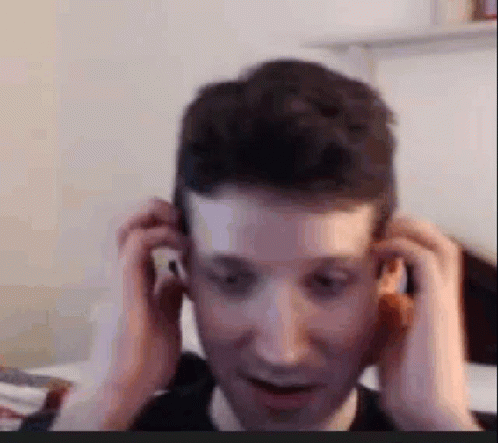 A Man Is Adjusting His Ear Buds While Sitting In Front Of A Computer Screen . GIF