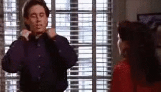 A Man Is Adjusting His Tie In Front Of A Woman In A Red Dress . GIF