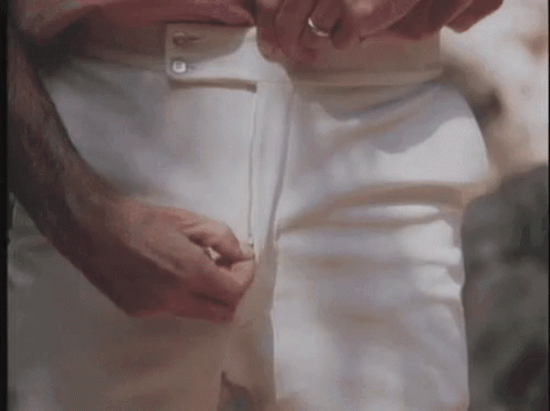 A Man Is Adjusting His White Pants While Wearing A Ring On His Finger . GIF