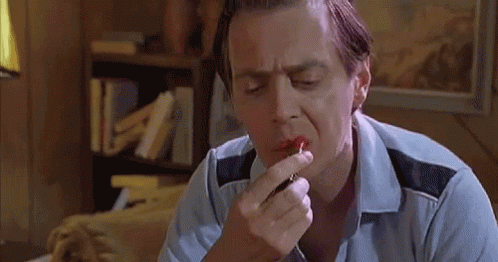 A Man Is Applying Red Lipstick To His Lips While Sitting Down . GIF