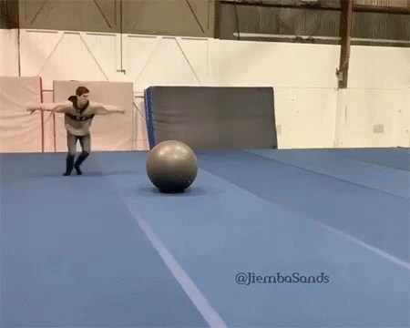 A Man Is Balancing A Ball On A Blue Mat With The Hashtag Jiembasands On The Bottom Right GIF
