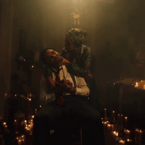 A Man Is Being Held By A Woman In A Dark Room With Candles GIF