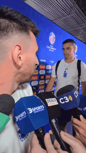 A Man Is Being Interviewed By Several Microphones Including A Sports One GIF