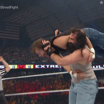 A Man Is Being Lifted In The Air By Another Man In A Wrestling Ring With A Star On The Bottom Right GIF
