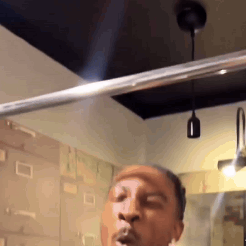 A Man Is Blowing A Kiss In A Bathroom With A Light Hanging From The Ceiling GIF