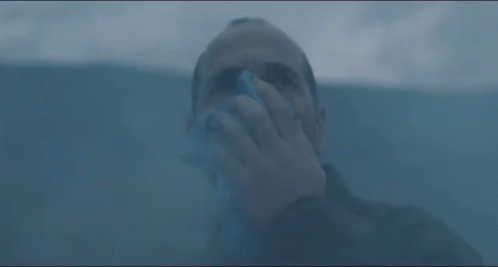 A Man Is Blowing His Nose With A Napkin While Standing In A Dark Room . GIF
