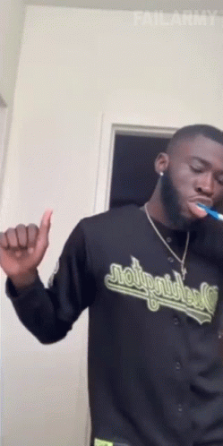 A Man Is Brushing His Teeth And Wearing A Jersey That Says Moto Riders GIF