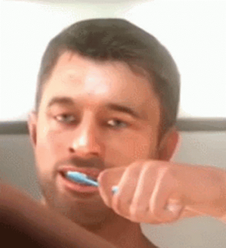 A Man Is Brushing His Teeth With A Blue Toothbrush In Front Of A Mirror . GIF