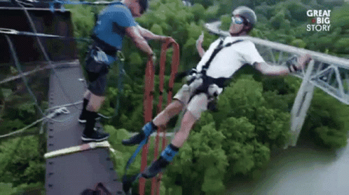 A Man Is Bungee Jumping Off A Bridge While Another Man Helps Him . GIF