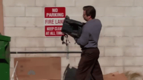 A Man Is Carrying A Bag In Front Of A No Parking Sign GIF
