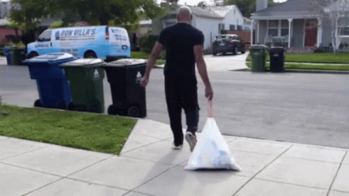 A Man Is Carrying A Bag Of Trash Down A Sidewalk In Front Of A Don Villas Van GIF