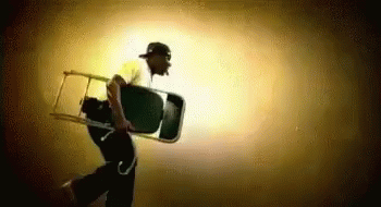 A Man Is Carrying A Chair On His Back In The Dark . GIF