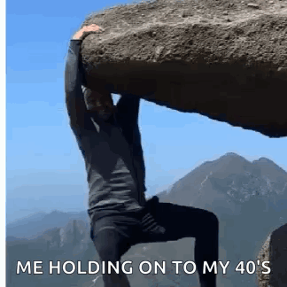A Man Is Carrying A Large Rock On His Shoulders . GIF