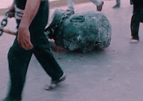 A Man Is Carrying A Large Rock With Chains Around It . GIF