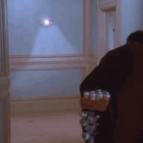 A Man Is Carrying A Tray Of Cans In A Hallway GIF