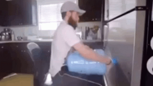 A Man Is Carrying A Water Bottle On His Back Into A Refrigerator . GIF