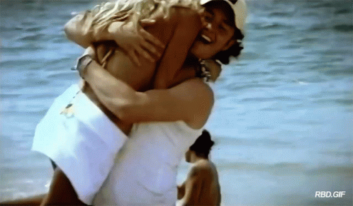 A Man Is Carrying A Woman In His Arms On The Beach With Rbd.gif Written On The Bottom GIF