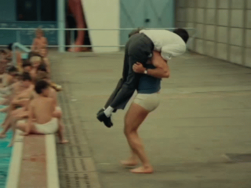 A Man Is Carrying A Woman Into A Pool GIF