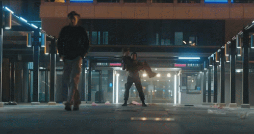 A Man Is Carrying Another Man In His Arms In A Building With A Sign That Says Donuts GIF