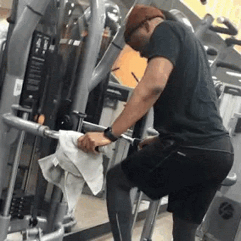 A Man Is Cleaning A Exercise Machine In A Gym With A Towel . GIF