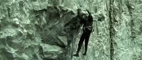 A Man Is Climbing A Rock Wall With A Rope . GIF