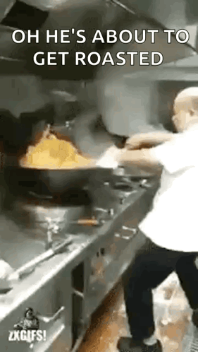 A Man Is Cooking Food In A Kitchen With A Frying Pan Filled With Food And A Fire Coming Out Of It . GIF