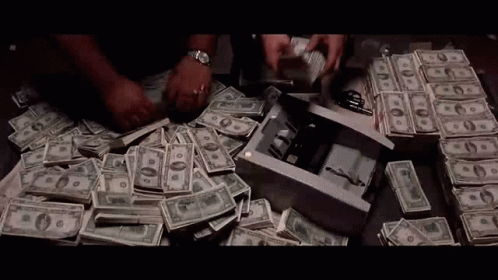 A Man Is Counting Money On A Table With A Bunch Of Money On It . GIF