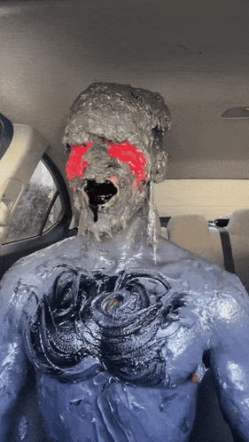 A Man Is Covered In A Thick Gray Substance With Red Paint On His Face GIF