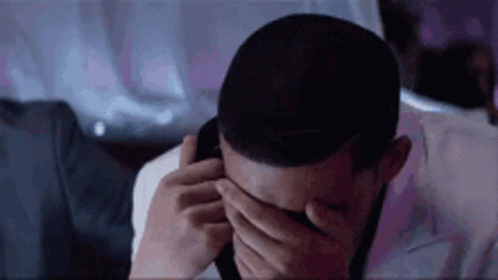 A Man Is Covering His Eyes With His Hands While Talking On A Cell Phone . GIF