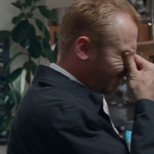 A Man Is Covering His Eyes With His Hands While Wearing A Jacket And Tie . GIF