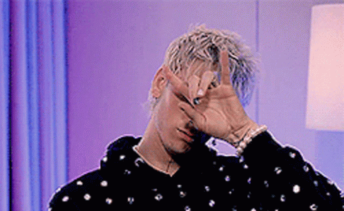 A Man Is Covering His Face With His Hand And Making A Peace Sign . GIF